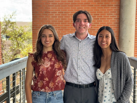 Three people stand in front of a brick wall.