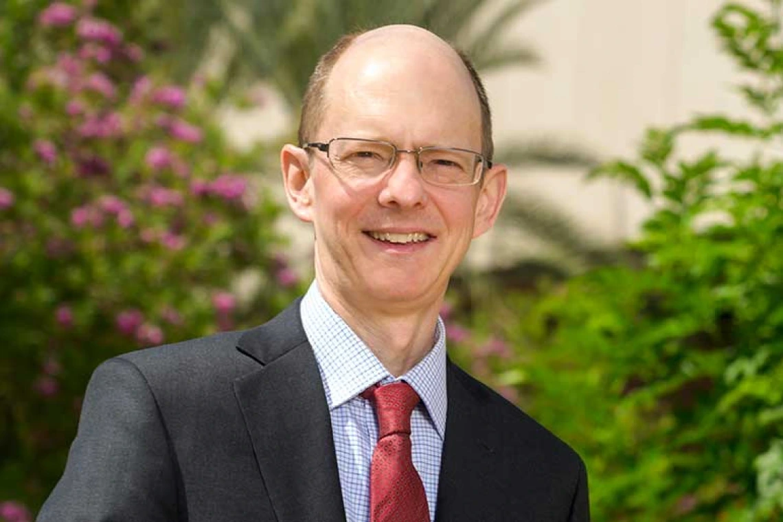 A bespectacled man in a suit and tie smiles for a portrait.