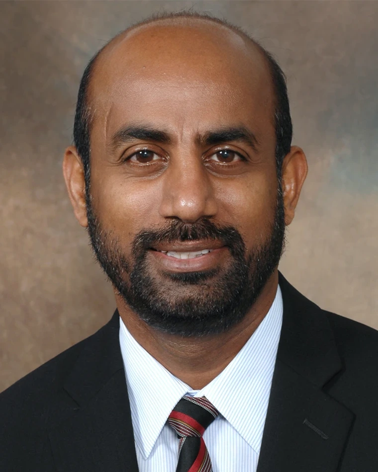 portrait of person with dark hair and beard, wearing suit and tie