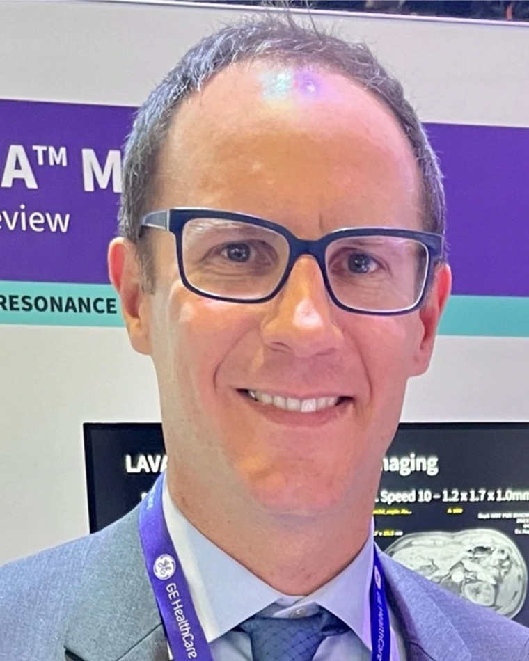 person with short gray hair, wearing glasses, shirt, jacket, tie and lanyard