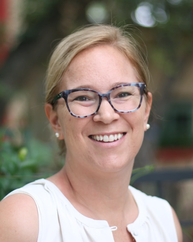person with short blonde hair, wearing glasses, earrings and white shirt