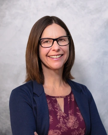 Person wearing glasses and a navy sweater, smiling