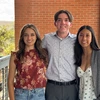 Three people stand in front of a brick wall.